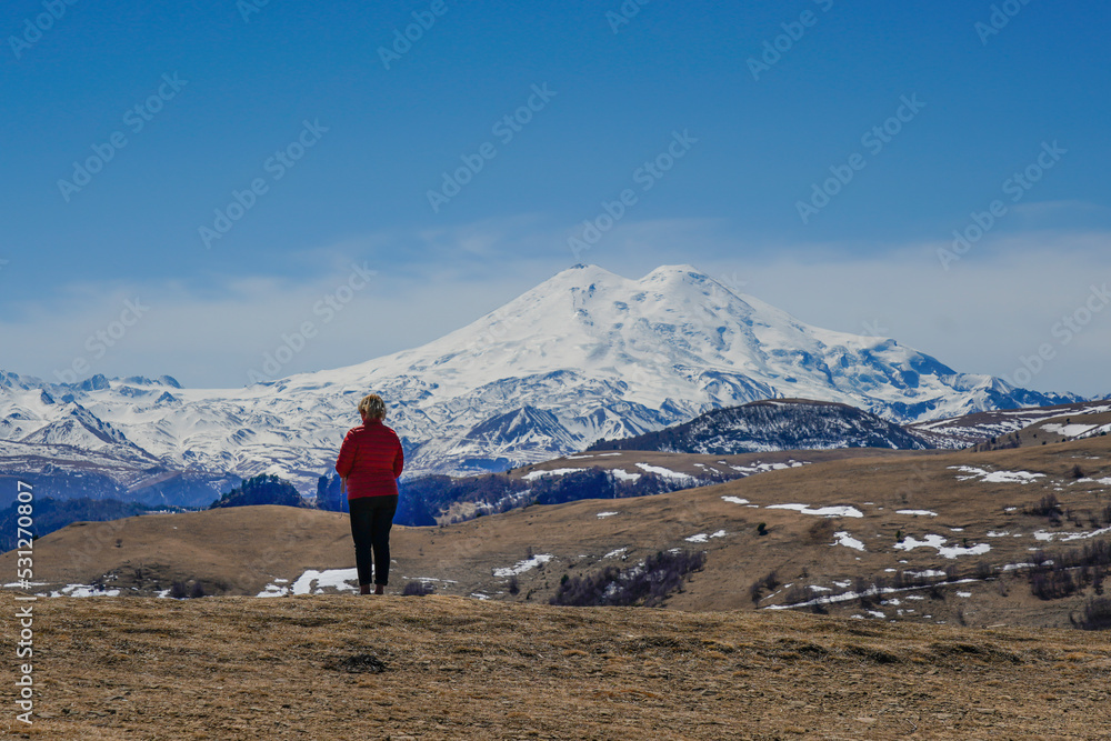 Panorama of Mount Elbrus against the backdrop of the Main Caucasian Range. bckview of a woman, Karachay-Cherkessia. Russia.