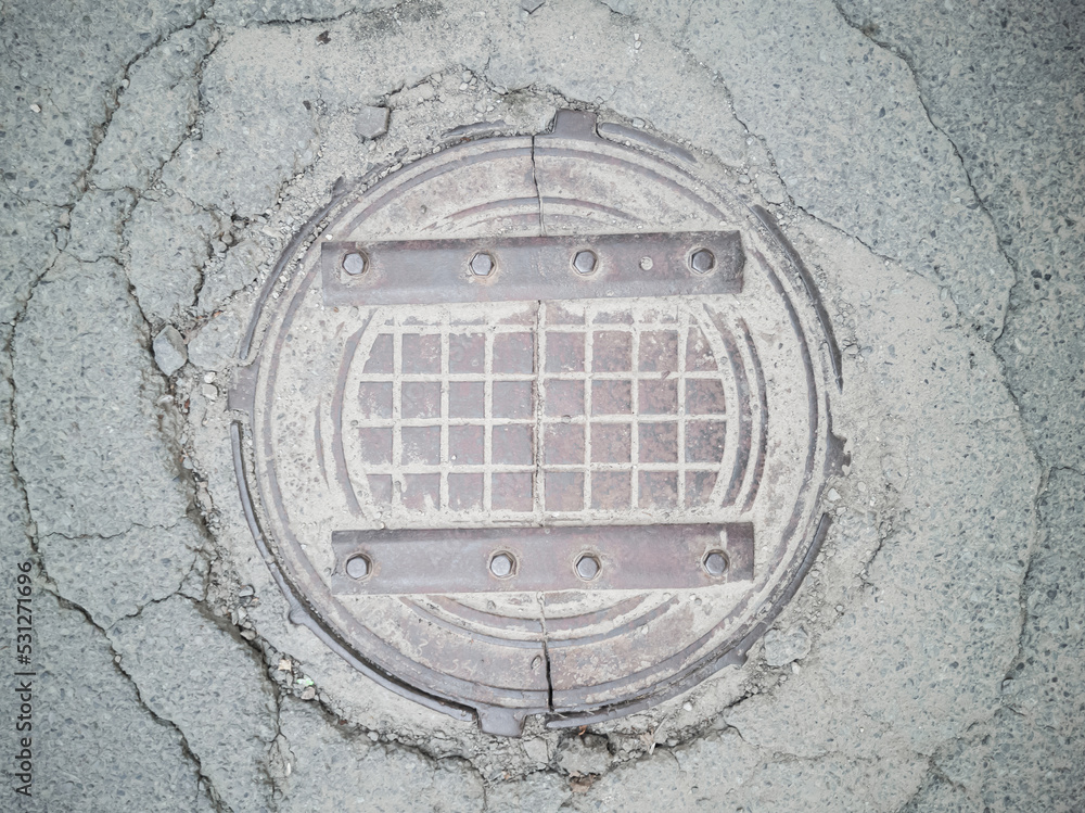 An old cracked in half metal manhole cover on an abandoned asphalt road. Top view. Textured. An old cracked in half metal manhole cover on an abandoned asphalt road. Top view. Textured.