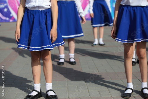 A group of little girls dancers performing at the festival in costumes blue short skirt and black shoes on the square outdoors on a summer day