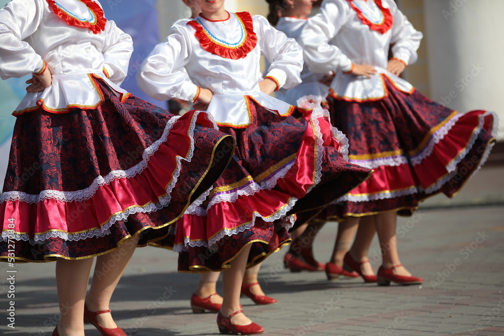 A female group dancing in a colorful folklore red and white costume performs at an outdoor celebration on a sunny day