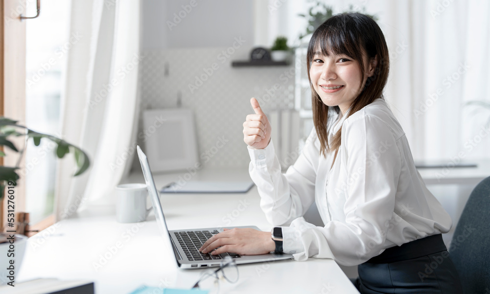 Young Asian businesswoman working on laptop and raised thumb up motivate herself with confident Young Asian businesswoman working on laptop and raised thumb up motivate herself with confident