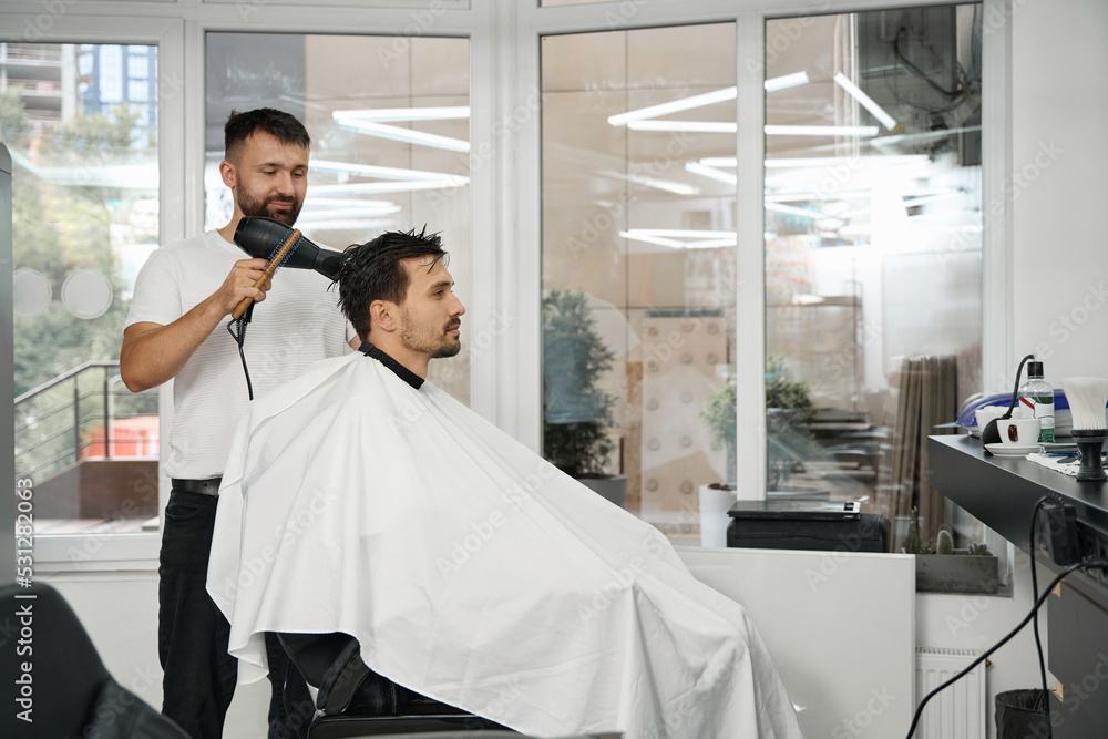 Hair salon worker with hairdryer standing next to client Hair salon worker with hairdryer standing next to client