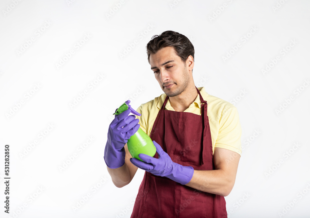 Handsome serious male contractor from cleaning service in red apron and violet rubber gloves holding cleaning tools isolated on white background Handsome serious male contractor from cleaning service in red apron and violet rubber gloves holding cleaning tools isolated on white background