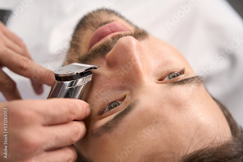 Attractive young gentleman using service of barber for moustache trim