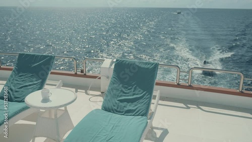Selective focus on daybeds on the upper deck of a moving luxury diving safari yacht with a small coffee table in between and the ocean horizon in the background with two more vessels behind