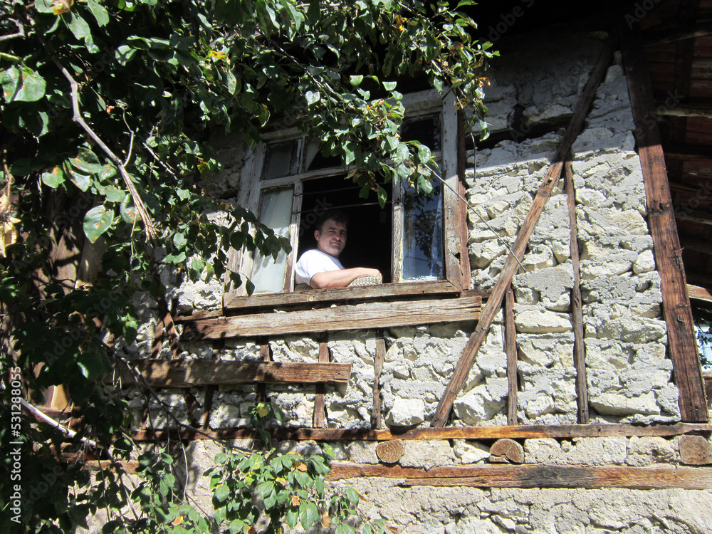    middle-aged man looking through window in old house