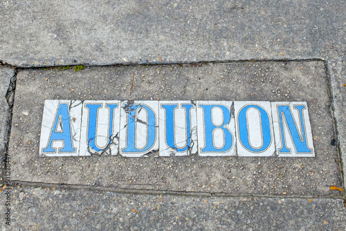 Cracked and broken traditional Audubon Street tile inlay street sign on sidewalk in Uptown Neighborhood in New Orleans, Louisiana, USA