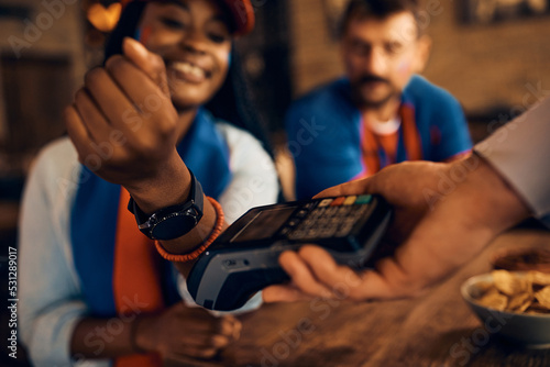 Close up of black sports fan using her smart watch while paying contactless in pub