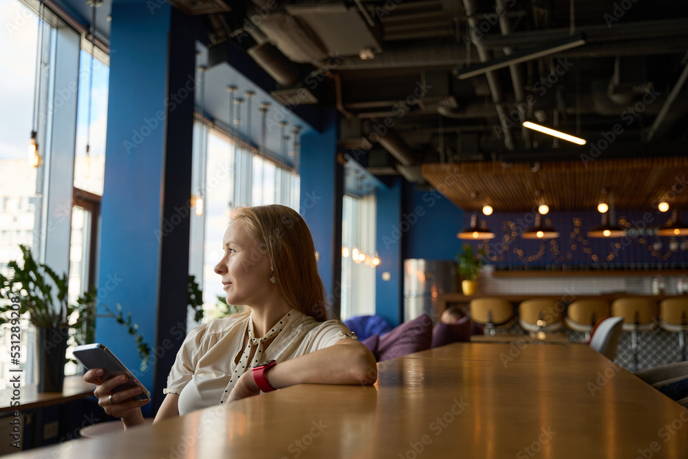 Woman sits at bar table with a phone in hands