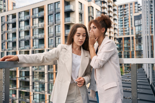 Office worker telling secret to her colleague outside