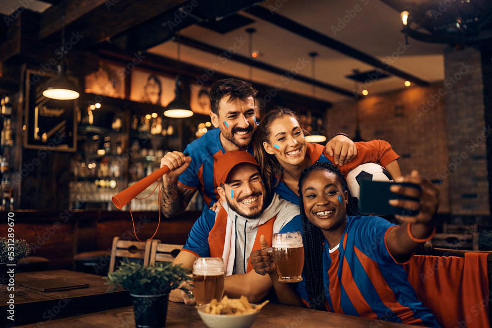 Cheerful group of soccer fans taking selfie while having fun in pub.