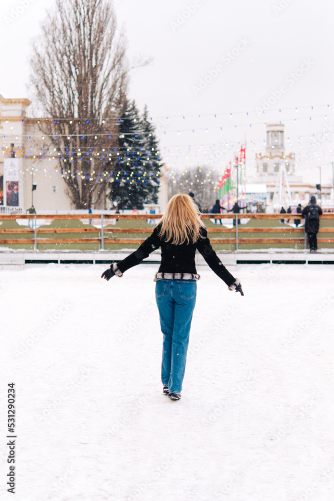 Woman walks outdoors in winter. Warm clothes in cold weather. Woman in a fur coat and jeans. Rest in winter city amusement park