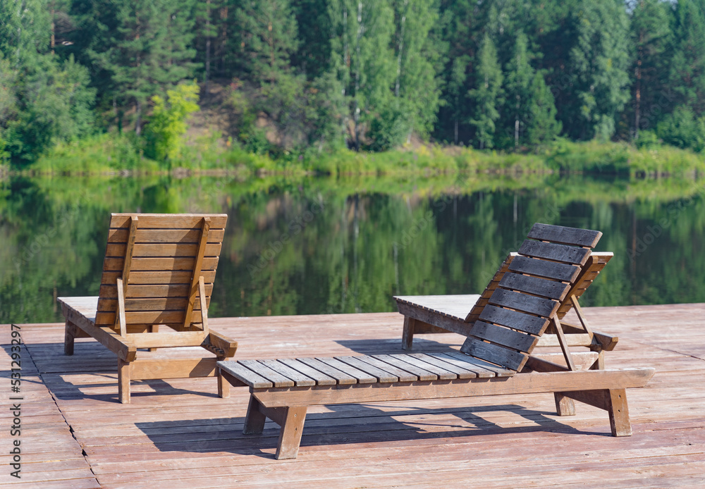 The hotel's terrace with wooden sun loungers is located on the shore of a lake surrounded by a forest. The hotel's terrace with wooden sun loungers is located on the shore of a lake surrounded by a forest.