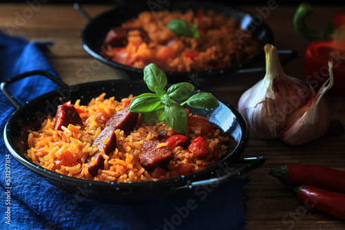 Spanish food specialty - chorizo sausage cooked with rice, tomatio, paprika, onion, garlic and saasoned with smoked paprika powder - basil leaf decoration on top (dark and moody photography) photo