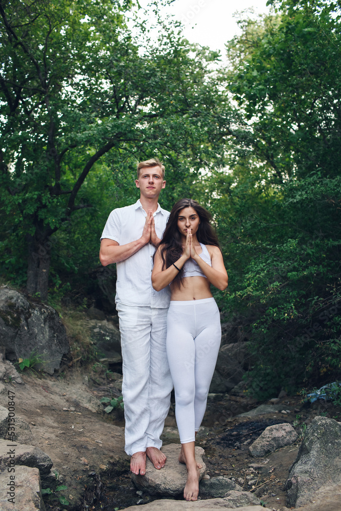 Couple doing yoga outdoors in nature. Woman and man meditate together in the morning. The concept of a positive mind. Couple doing yoga outdoors in nature. Woman and man meditate together in the morning. The concept of a positive mind.