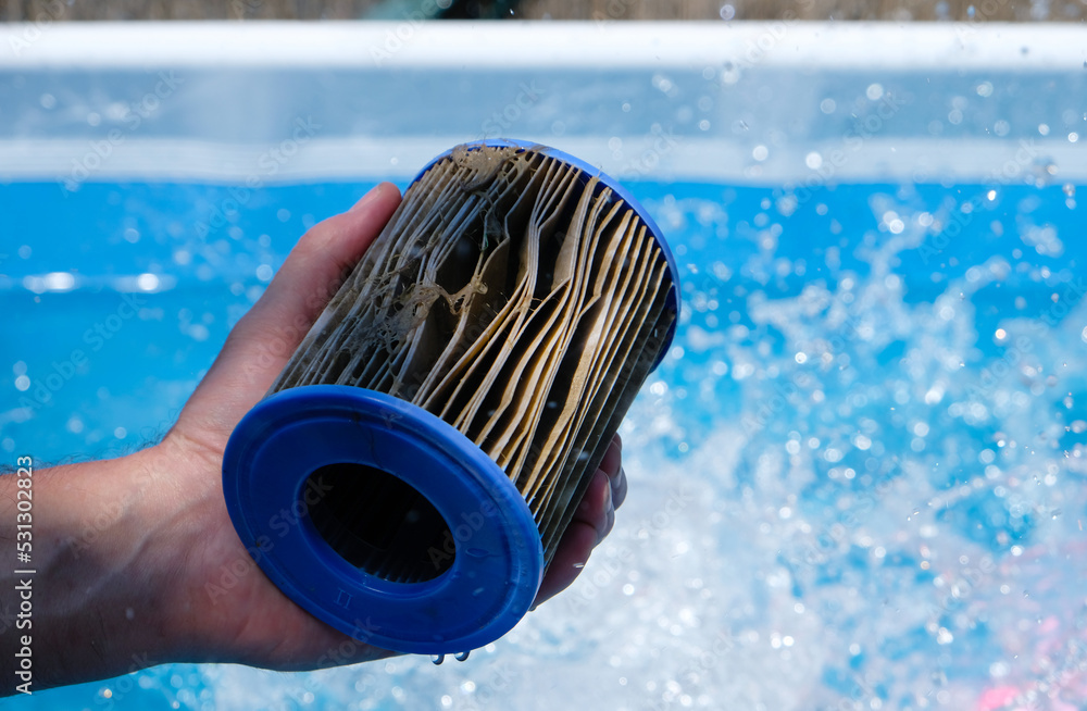 Dirty Replacement Pool Filter Cartridge in a man's hand on water splash