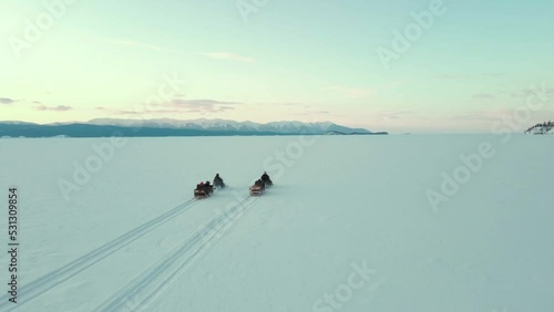 cinematic turnig around the couple of snowmobile riding in the winter landscape of the frozen lake Baikal photo