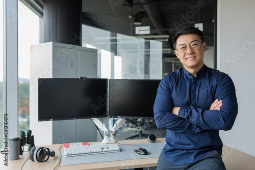 Portrait of successful programmer in modern office of development company, asian man with crossed arms smiling and looking at camera.