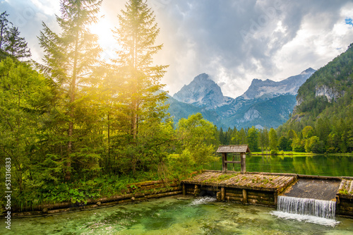 Famous green lake Schiederweiher near village Hinterstoder. Small weir and dam on lake with flowing water. Big Austrian mountains in background. Soft and magical colors in pure nature.