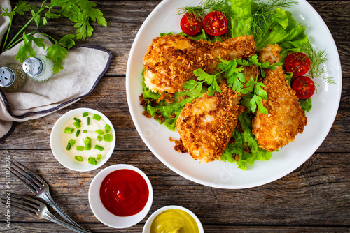 Panko crusted baked chicken drumsticks with greens on wooden table
 photo
