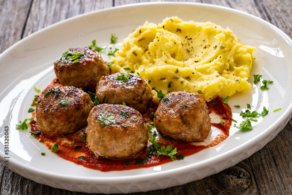 Fried pork meatballs with potato puree and tomato sauce on wooden table
