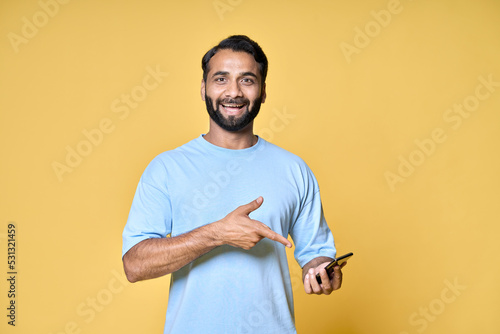 Print op canvas Happy amazed indian man holding cell phone pointing at smartphone isolated on yellow background advertising betting, new game or music app, online ecommerce shop sale offer