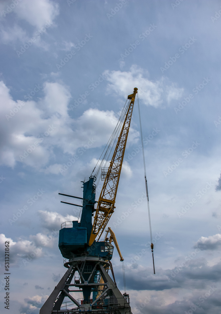 Large tower cranes stand in a river port against a cloudy sky.