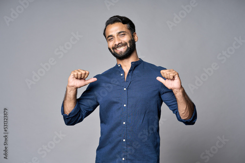 Smiling proud confident indian professional business man standing isolated on gray background pointing at himself bragging as choose me concept. Human resources, self-confidence, ego. Portrait.