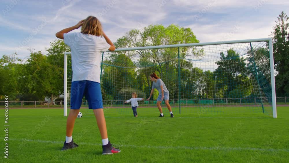 Happy family with two children playing with a soccer ball throwing the ball to each other. Happy family with football ball on a field Happy family with two children playing with a soccer ball throwing the ball to each other. Happy family with football ball on a field