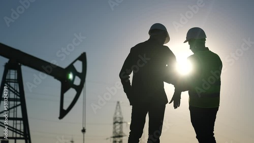 oil production. two silhouette workers work as a team next to an oil pump. business oil production production concept. two engineers of the oil and gas industry are discussing a sun business plan photo