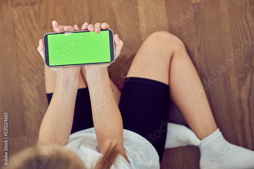 Children's hands using a phone with a green screen. A little girl is sitting on the floor and holding a smartphone with a chromakey. High quality photo
