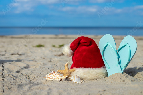 Christmas background Santa Claus hat on the beach with starfish and beach slippers