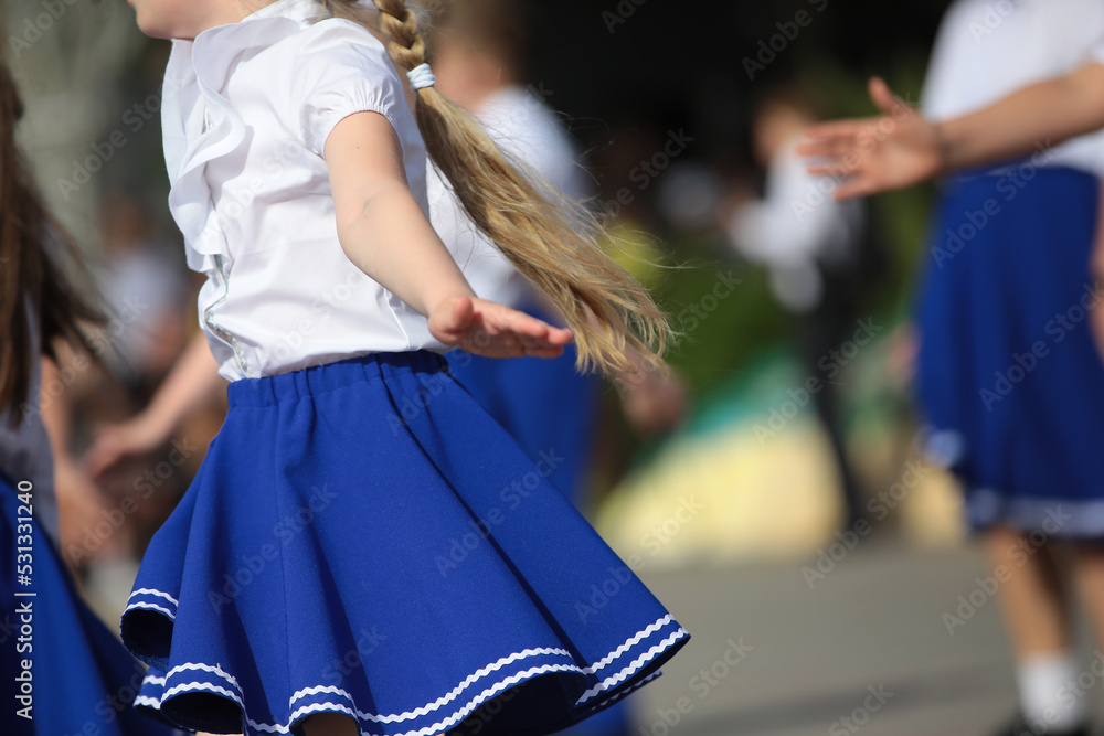 A group of little girls dancers in costumes performing at an outdoor celebration on a summer day.The view of a young performer in active motion with developing long hair.Children leisure concept