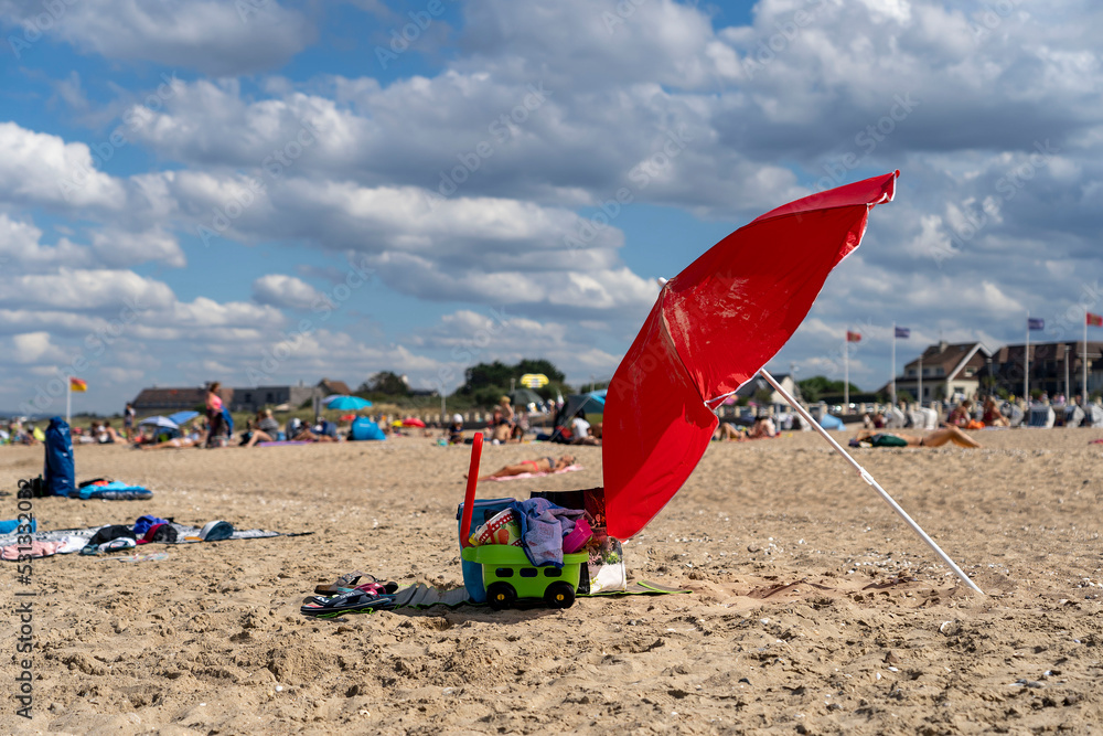 Red beach umbrella close-up. Wide sandy beach of the English Channel coast in Normandy on a summer day. Merville-Franceville-Plage, Normandy, France.