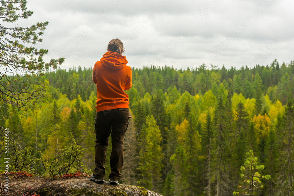 Naklejka premium a woman in a hoodie and trousers stands on the edge of a cliff against the background of a forest. the concept of travel and tourism