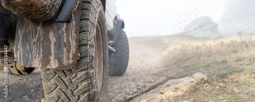 Obraz na plátně Close-up detail bottom POV view of 4x4 awd suv vehicle on dirt gravel unpaved road in autumn at misty mountain top