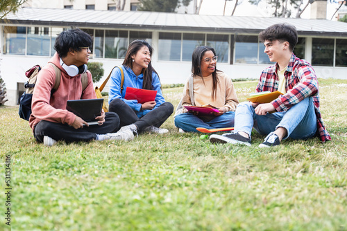 University student friends sitting on the grass, talking and sharing moments in the college campus. Asian African American youth
