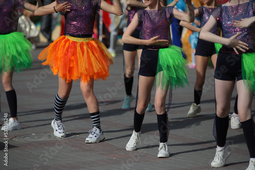 A group of happy girls are doing fitness exercises to the music dancing on a holiday in bright costumes outside on a summer day.The concept of sports and recreation for young people