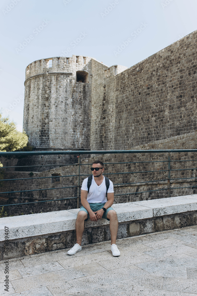 Man  sits at one of the entrance Facade gates to the old walled town Dubrovnik, Croatia. Fortress controlling and protecting the port. capital Seven Kingdoms, show Game of Thrones. Traveling, tourism