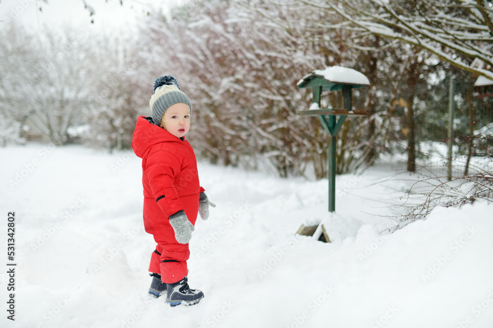 Adorable toddler boy having fun in snow covered park on chilly winter day. Child exploring nature.