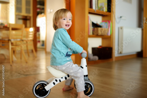 Funny toddler boy riding a baby scooter at home. Kid training balance on mini bike indoors. photo