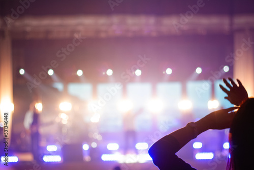Defocus silhouette of one woman raise hand up in music concert with purple and white color spotlight on stage background. Copy space. Out of focus