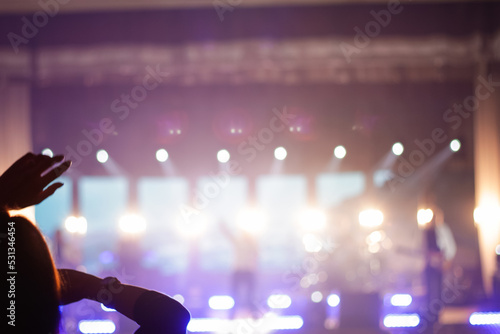 Defocus silhouette of one woman raise hand up in music concert with purple and white color spotlight on stage background. Copy space. Design. Out of focus
