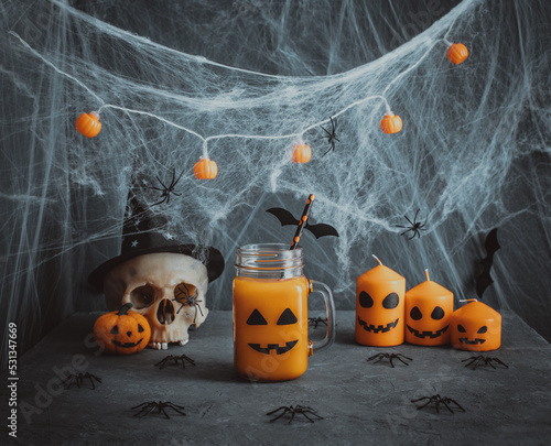 Halloween party decorations. Pumpkin juice with a jack-o-lantern face  cobwebs  candles and a skull on a dark background. Halloween drink.