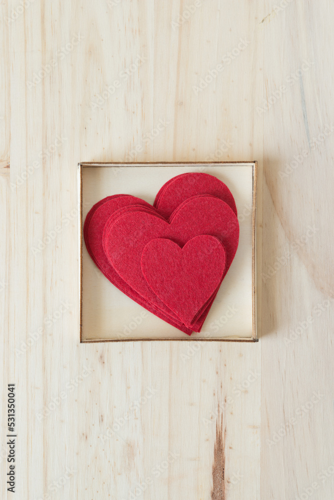 pile of felt hearts in a box on a wood surface pile of felt hearts in a box on a wood surface
