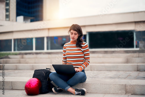 latin young woman sitting outdoors on the stairs with a laptop and a bag working