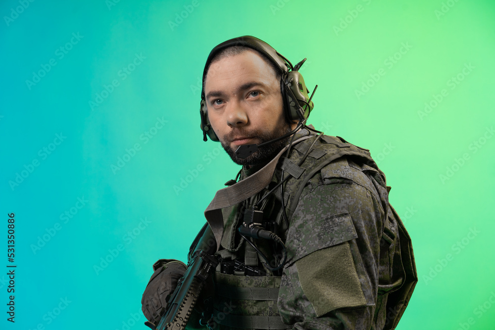 soldier in the studio on a green background with colored light. a man in military uniform with a gun, rifle or machine gun. military. airball player soldier in the studio on a green background with colored light. a man in military uniform with a gun, rifle or machine gun. military. airball player