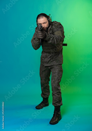 soldier in the studio on a green background with colored light. a man in military uniform with a gun, rifle or machine gun. military. airball player