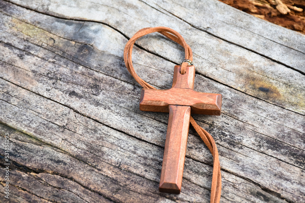 A wooden cross with a light brown leather strap rests on a wooden floor. A wooden cross with a light brown leather strap rests on a wooden floor.