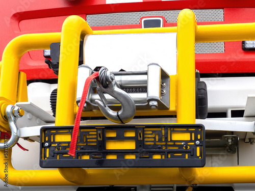 Winch on rescue vehicle. Fragment of body of fire truck. Steel hook on car winch. Winch for rescue operations. Yellow metal frame on firetruck. Automobile emergency fragment. Frame for car number